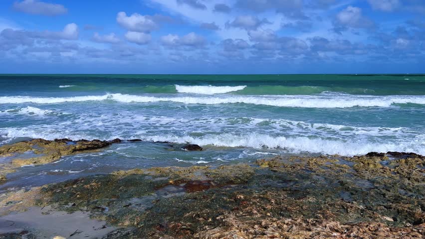 Rocky Cuban beach in Varadero, Cuba, on a cloudy day, when the sun breaks through the clouds, you can see the waves and ocean expanses. Turquoise waves. Stone slabs on the beach in the ocean. 4K	