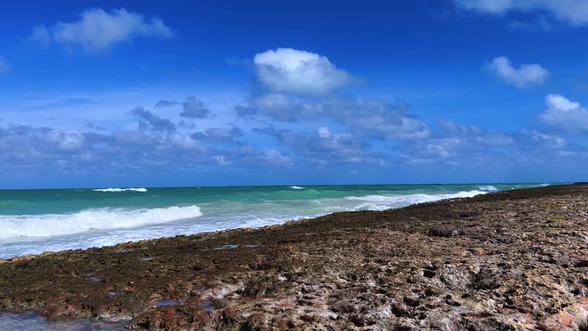 Rocky Cuban beach in Varadero, Cuba, on a cloudy day, when the sun breaks through the clouds, you can see the waves and ocean expanses. Turquoise waves. Stone slabs on the beach in the ocean. 4K	