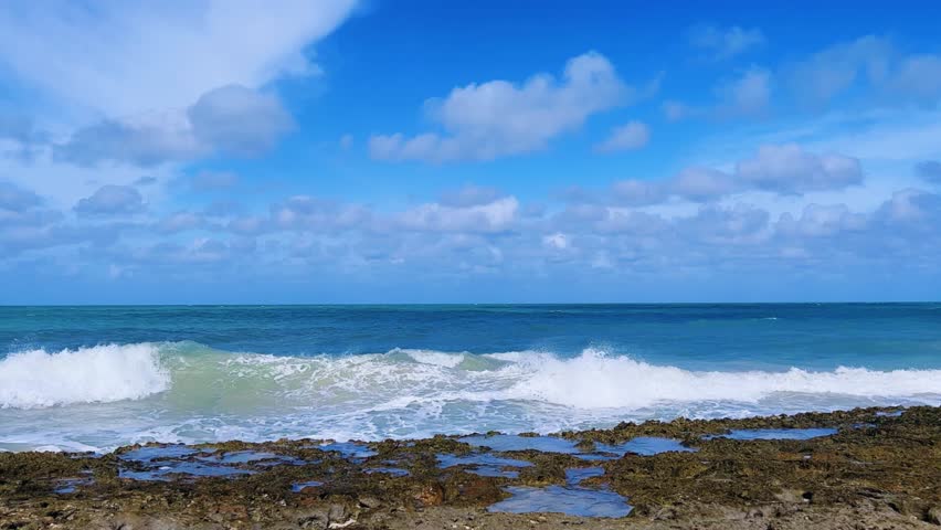 Rocky Cuban beach in Varadero, Cuba, on a cloudy day, when the sun breaks through the clouds, you can see the waves and ocean expanses. Turquoise waves. Stone slabs on the beach in the ocean. 4K	