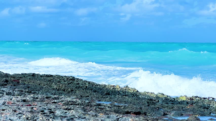Rocky Cuban beach in Varadero, Cuba, on a cloudy day, when the sun breaks through the clouds, you can see the waves and ocean expanses. Turquoise waves. Stone slabs on the beach in the ocean. 4K	