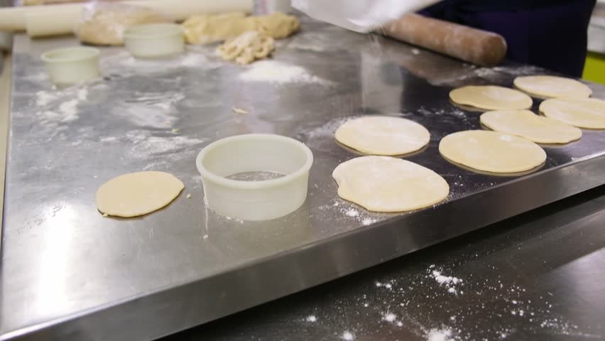 Preparing dough discs: hands crafting pastry with cookie cutter and rolling pin.