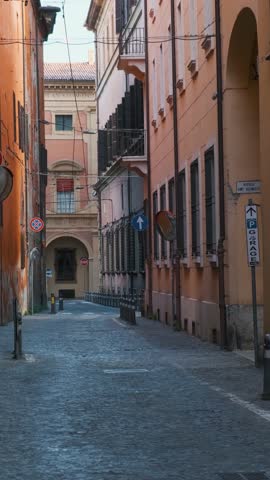 Medieval narrow street with nobody in Bologna old town, Emilia Romagna, Italy at sunrise. Italian street with colorful building facades. Vertical orientation. Travel destination in Europe
