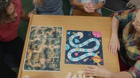 Medium top view of Caucasian family - mother, father, son and daughter playing roll and move game at table at home, shaking and throwing dice, moving checker over colourful field - Powered by Shutterstock - Get 15% off with code: PIKWIZARD15