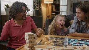 Medium shot of cheerful Caucasian father with limb difference disability playing roll and move game with wife, son and daughter at home, shaking, throwing dice, moving checker on field - Powered by Shutterstock - Get 15% off with code: PIKWIZARD15
