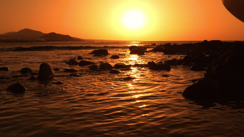 SILHOUETTE, LENS FLARE: Woman with surfboard in her hand crosses shimmering shallows in golden light as she heads towards the waves. Female surfer in bikini is going for an early morning surf session.