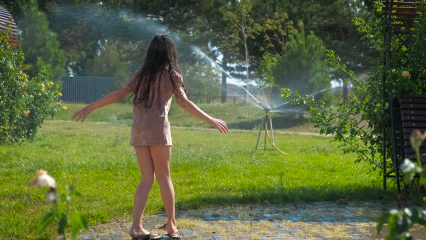 little girlin water sprinkles in the garden. A view of child relax in water sprinkle in the summer park during weekend time.
