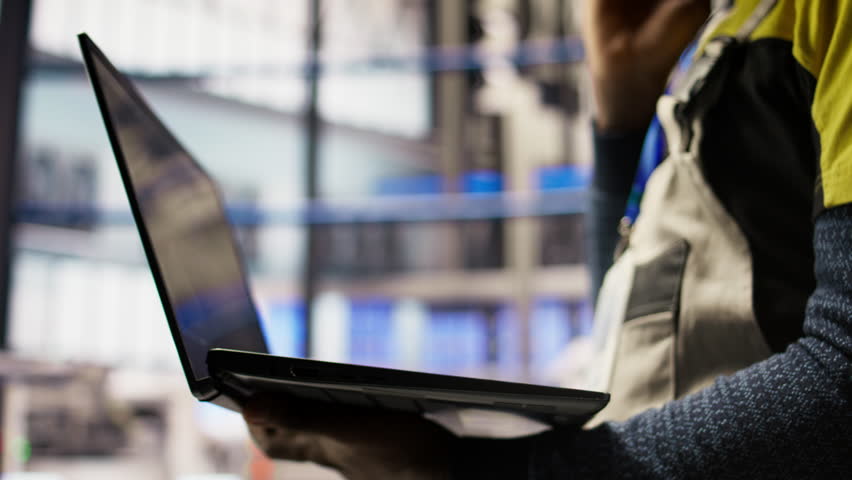 Close up of smart factory worker using laptop to test automated systems, monitoring production metrics. Industry 4.0 plant expert inspecting machinery to identify and fix malfunctions, camera A