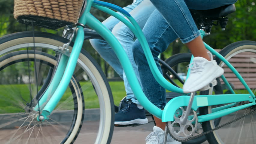 A couple rides bicycles through a vibrant park, enjoying the outdoors. The sun shines brightly as they cruise along the path, feeling the freedom of the moment.