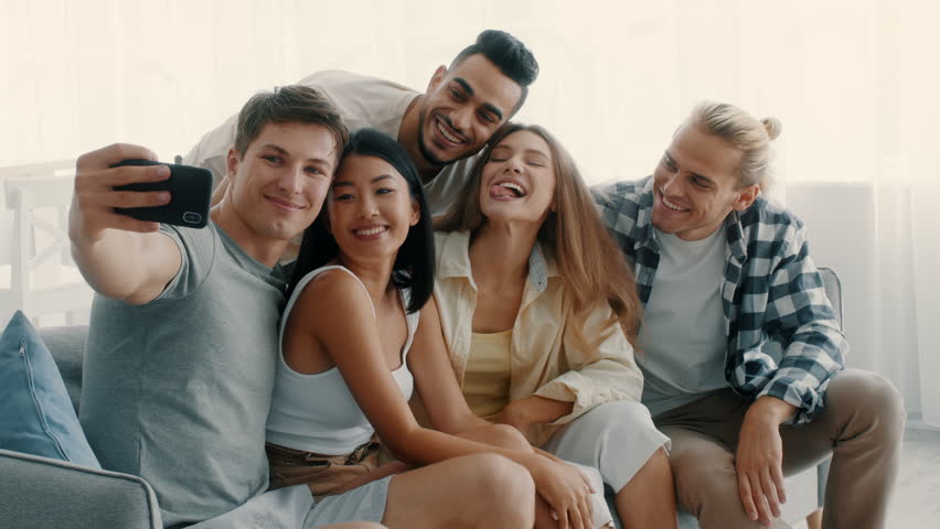 Five diverse friends gather for a fun day at home, sharing laughter and playful selfies. They enjoy each other's company while creating lasting memories in a relaxed atmosphere.