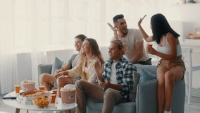 A group of diverse friends gathers in a cozy living room to watch a game. They cheer excitedly, holding snacks and drinks, creating a fun and lively atmosphere together. - Powered by Shutterstock - Get 15% off with code: PIKWIZARD15