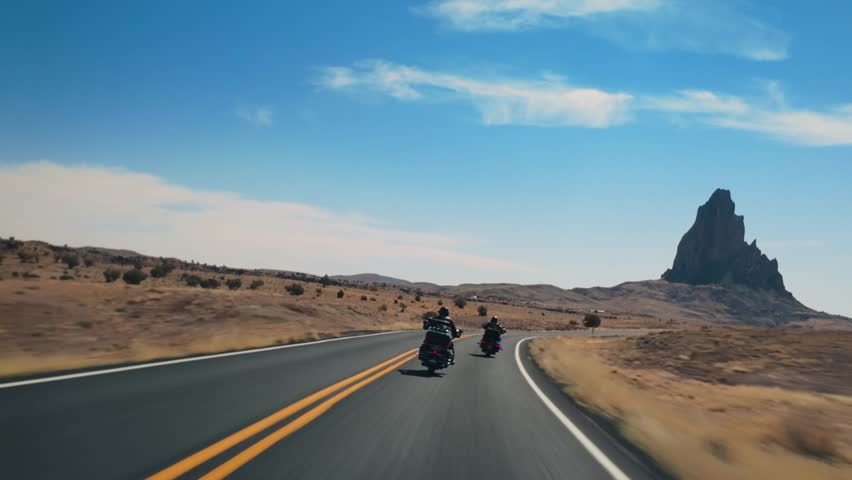 A couple of adventurous motorcyclists ride along the picturesque and scenic roads of Monument Valley, showcasing the breathtaking and stunning landscapes found in Arizona and Utah, two iconic states