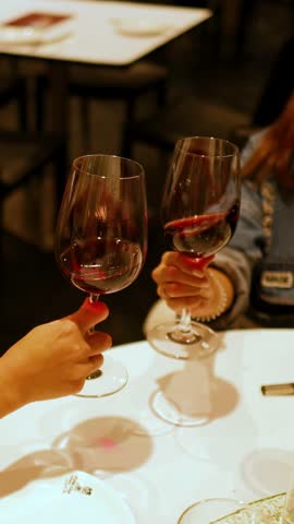Two people clink glasses of red wine in a warmly lit restaurant, creating a celebratory and intimate atmosphere