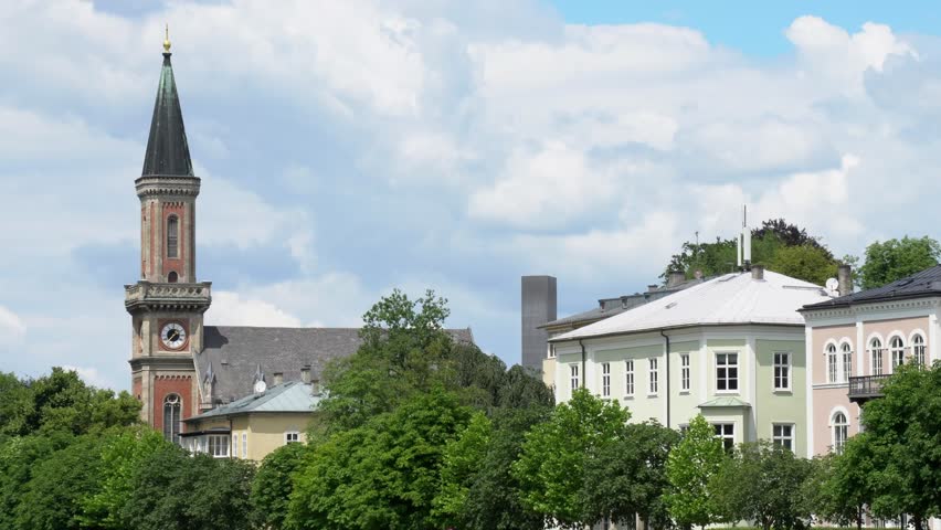 A picturesque church tower and colorful historic buildings surrounded by lush greenery in Salzburg, Austria.