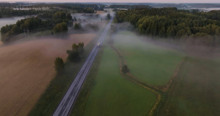 Aerial view following a truck on a foggy countryside road, misty morning