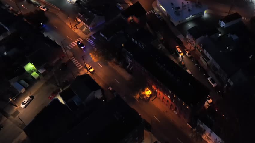 Blinking blue and red lights of police car driving on street at night. Orange lighting lantern along Main Street of city. Tracking drone shot.