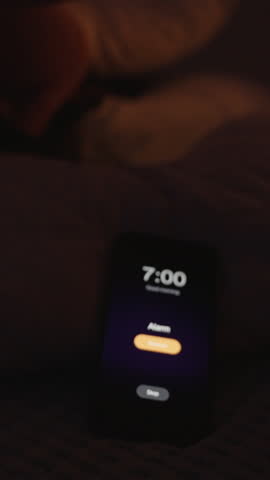 Vertical video. Lonely Woman Covers Face with Pillow and Reaches for Smartphone to Turn Off 7 AM Alarm in Dark Room, Close-Up Low Angle, Reluctant Wake-Up Concept