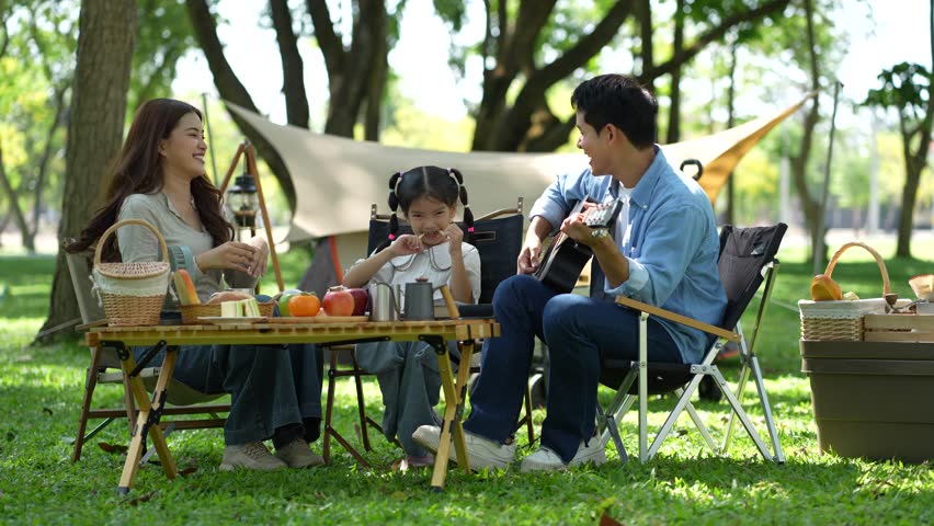 Asian family enjoying a picnic in the park on a sunny weekend. Smiling parents and kids bonding, relaxing, and spending joyful time together in nature.