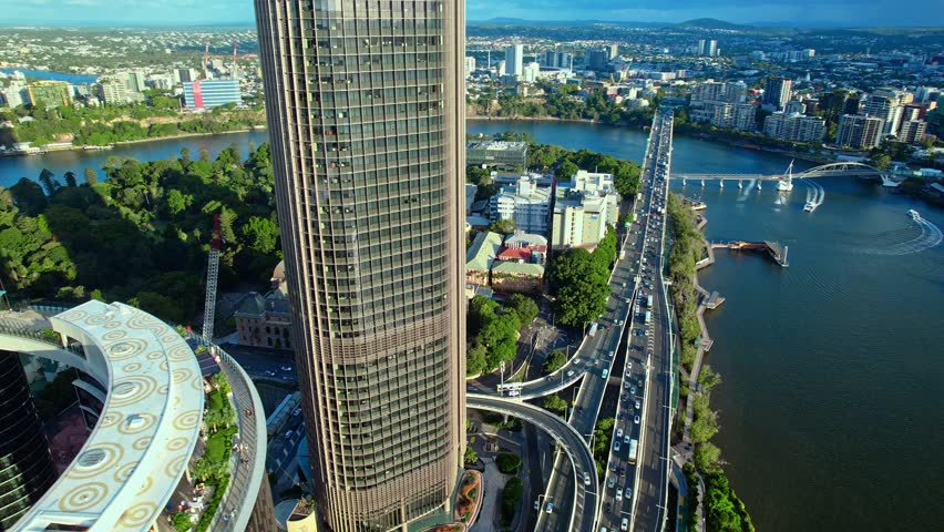Aerial footage of a modern urban landscape featuring glass skyscrapers, a high-speed highway, and a scenic city riverfront. Captured in Brisbane, Australia