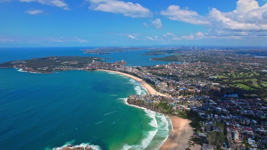 A spectacular aerial view of Sydney s coastline, featuring a stunning crescent-shaped beach with golden sands and turquoise waters. The image captures the lush greenery, residential areas
