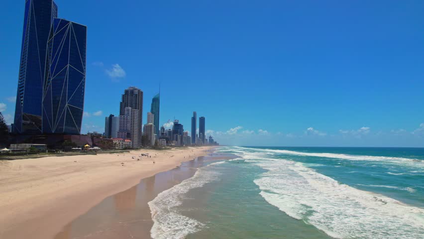 A drone soars over Gold Coast's turquoise waves, capturing towering skyscrapers lining the shore and sunbathers dotting golden sands. This vibrant aerial view