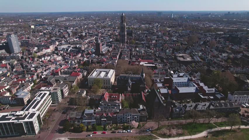 Panoramic aerial approach of De Dom medieval cathedral tower in scaffolding in Dutch city center of Utrecht towering over the cityscape against a blue sky sunrise and orange glow on the horizon