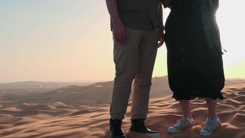 People stand on a desert sand dune in Dubai. The wind blows away the sand against the background of the sunset.