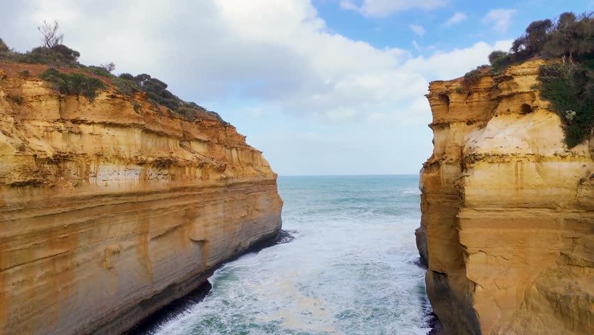 Drone footage captures the majestic cliffs and ocean waves at Loch Ard Gorge, Port Campbell, Australia, under bright daylight
