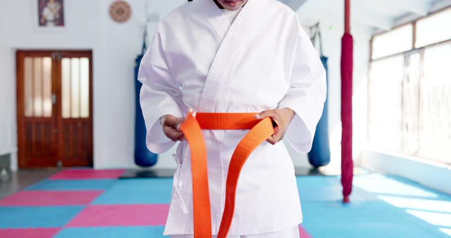 Person, hands and karate with orange belt for martial arts training, self defense or fighting skill level. Closeup, taekwondo or fighter getting ready with strap for promotion or experience in dojo