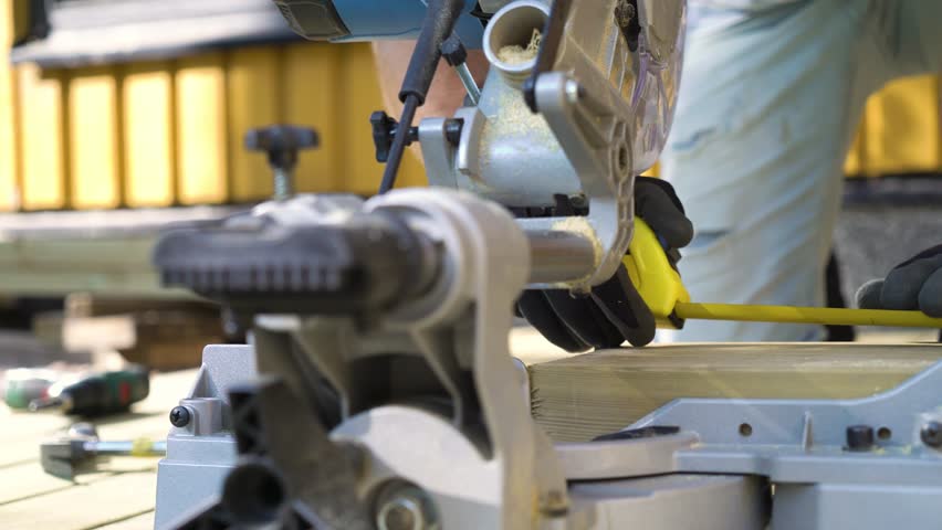 Close-up of a man using a circular saw to cut wood during an outdoor deck construction project, wearing protective gloves.