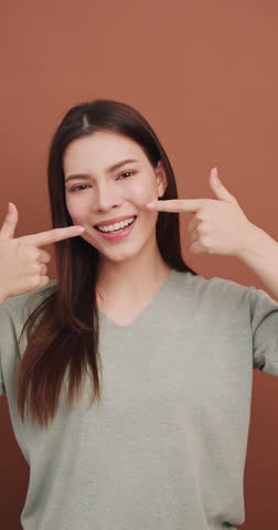 Vertical clip. Portrait of a young woman with healthy teeth. Isolated on brown background in studio.