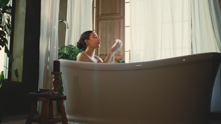 Woman taking bath at home or luxury hotel, SPA treatments for body and mind. Happy beautiful brunette female person playing with soap foam, enjoying calmness in sunday morning, lazy day in weekend
