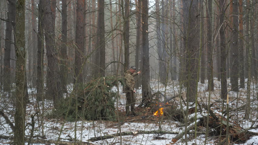 Bushcraft in a Snowy Forest with a Campfire, A man practices bushcraft skills in a snow-dusted forest, building shelter and tending to a fire