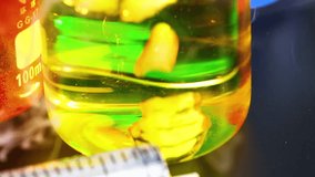 Close-up of yellow liquid with floating particles in a beaker, observed with a syringe nearby. - Powered by Shutterstock - Get 15% off with code: PIKWIZARD15