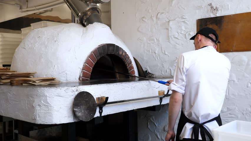 Italian pizza is cooked in a wood-burning oven. The chef holds a pizza spatula, the process of baking pizza in a traditional Italian oven. A firewood oven for cooking and baking pizza. - Powered by Shutterstock - Get 15% off with code: PIKWIZARD15