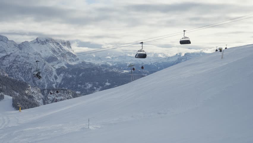 Ski gondolas glide up a pristine slope with rugged mountains stretching across the horizon. Parallax video.