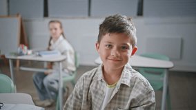 Portrait small kid sitting lesson in classroom. Smiling schoolboy listening teacher looking camera at cabinet closeup. Little happy boy learning in school auditorium. Joyful student schooling at desk - Powered by Shutterstock - Get 15% off with code: PIKWIZARD15