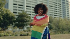 Portrait of smiling freedom woman wrapping with rainbow flag standing near commercial building. Positive African American female proud of LGBT community in urban area. Pride month - Powered by Shutterstock - Get 15% off with code: PIKWIZARD15