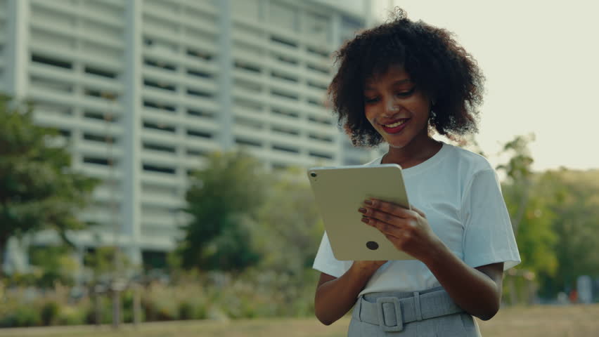 Portrait of pretty African American woman using tablet computer against office building on street. Female student scrolls internet in touchpad device on city square