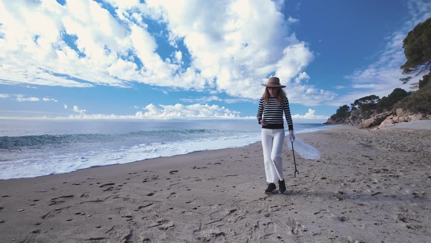 A middle-aged white woman takes a photo with her phone to report the plastic garbage littering the beach and littering the sand.