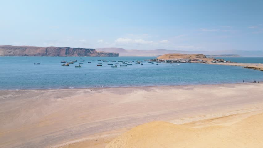 Aerial View of Fishing Boats Anchored in a Pacific Bay near Paracas Peninsula, Peru. Dozens of small boats, likely used for fishing, are anchored in calm waters, creating a picturesque maritime scene.