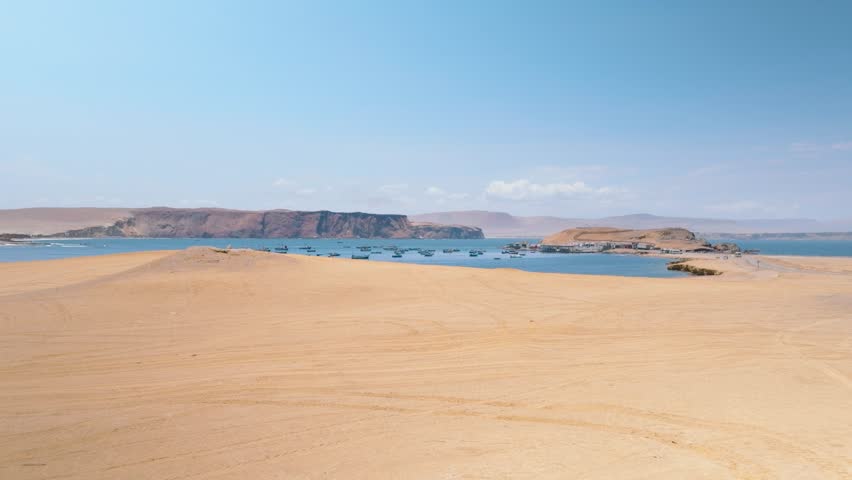 Aerial View of Fishing Boats Anchored in a Pacific Bay near Paracas Peninsula, Peru. Dozens of small boats, likely used for fishing, are anchored in calm waters, creating a picturesque maritime scene.