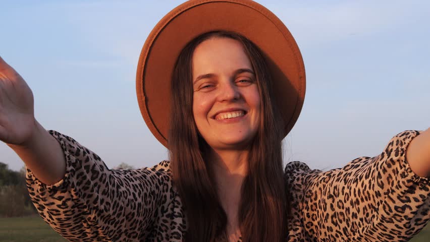 Woman in a stylish leopard print outfit joyfully stretches her arms wide, basking in the glow of the sunset against a serene background