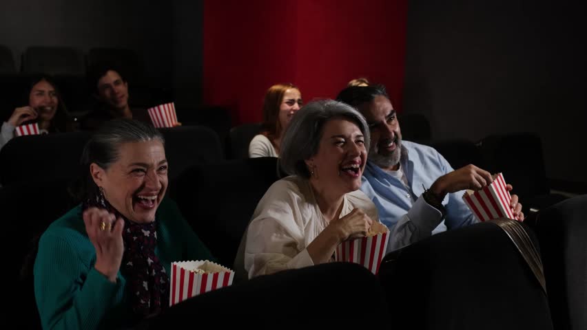Mature couple enjoying a funny movie at the cinema, laughing and eating popcorn