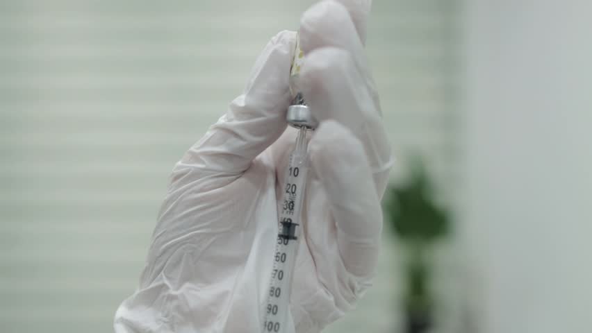 A doctor wearing gloves draws medication from a vial into a syringe, preparing for an injection. Ideal for medical, pharmaceutical, healthcare, and research-related projects.