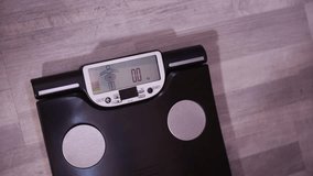 A woman stands on a smart scale to check her weight. The scale displays the weight in kilograms along with a body fat analysis icon. - Powered by Shutterstock - Get 15% off with code: PIKWIZARD15
