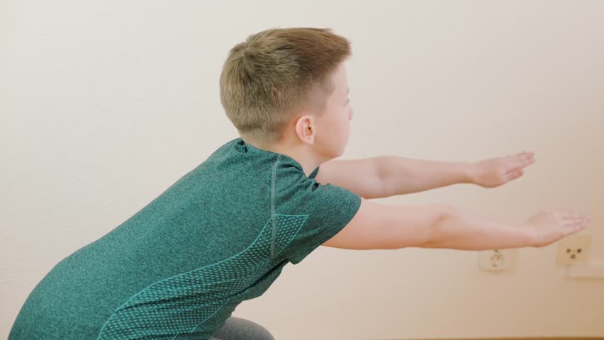 10-year-old boy squats at home, strengthening muscles and improving endurance, home gym, physical education, workout session, indoor fitness, sport exercises