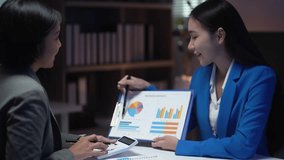 Two women are sitting at a table with a blue jacket on one of them. One of the women is holding a piece of paper with a pie chart on it. The other woman is holding a calculator - Powered by Shutterstock - Get 15% off with code: PIKWIZARD15