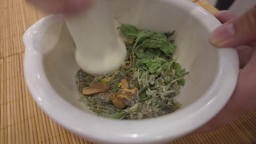 A close-up of hands grinding a natural blend of dried herbs and flowers using a mortar and pestle to create a handcrafted aromatic sachet.