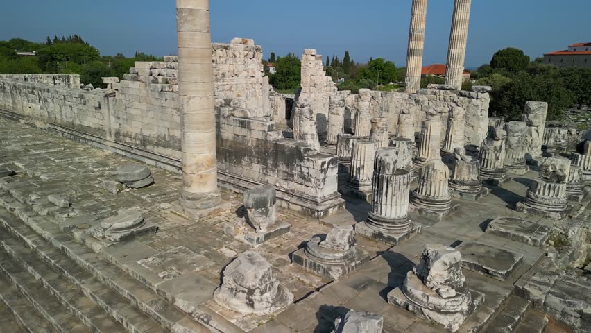 The Temple of Apollo in Didyma, Turkey seen from the sky. Majestic columns stand amidst ruins. The city and Aegean Sea shine in the distance under clear blue skies.