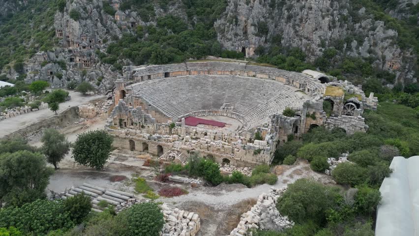 Amphitheater of Myra in Turkiye. Rock-cut tombs in cliffs. Roman theater surrounded by ruins. Drone view from above. Historical site in Turkey, well-preserved stone seats.